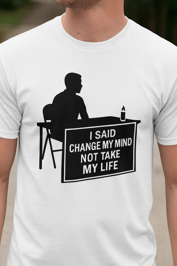 Man wearing a t-shirt with bold black silhouette artwork of a seated figure at a table with a lit candle. The sign on the table reads: 'I SAID CHANGE MY MIND NOT TAKE MY LIFE' — a tribute design honoring free speech and the legacy of Charlie Kirk.