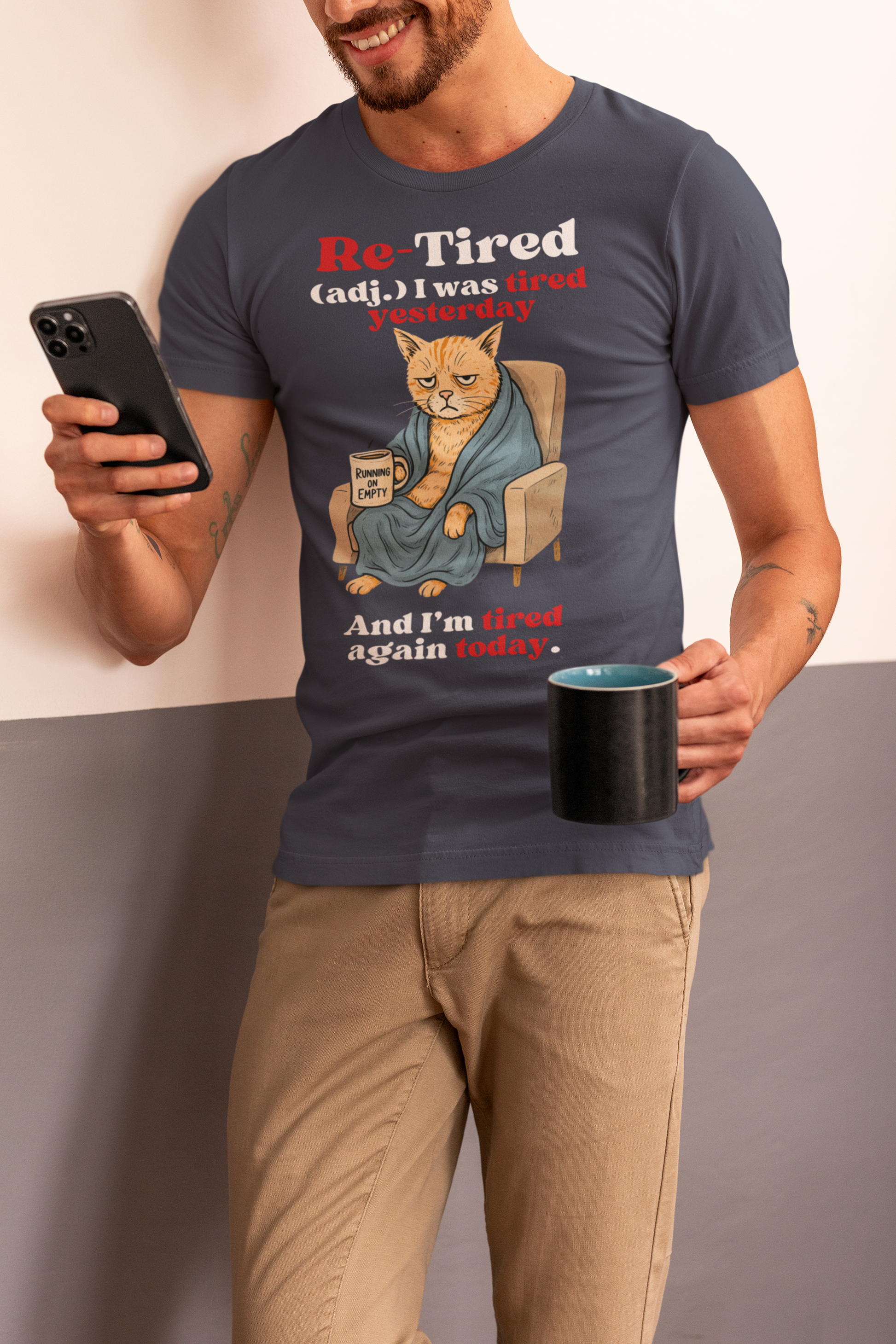 Man wearing a navy “Re-Tired” t-shirt featuring a grumpy orange cartoon cat wrapped in a robe and holding a “Running on Empty” coffee mug. Humorous Father’s Day shirt for tired dads, cat lovers, or sarcastic pet dads.